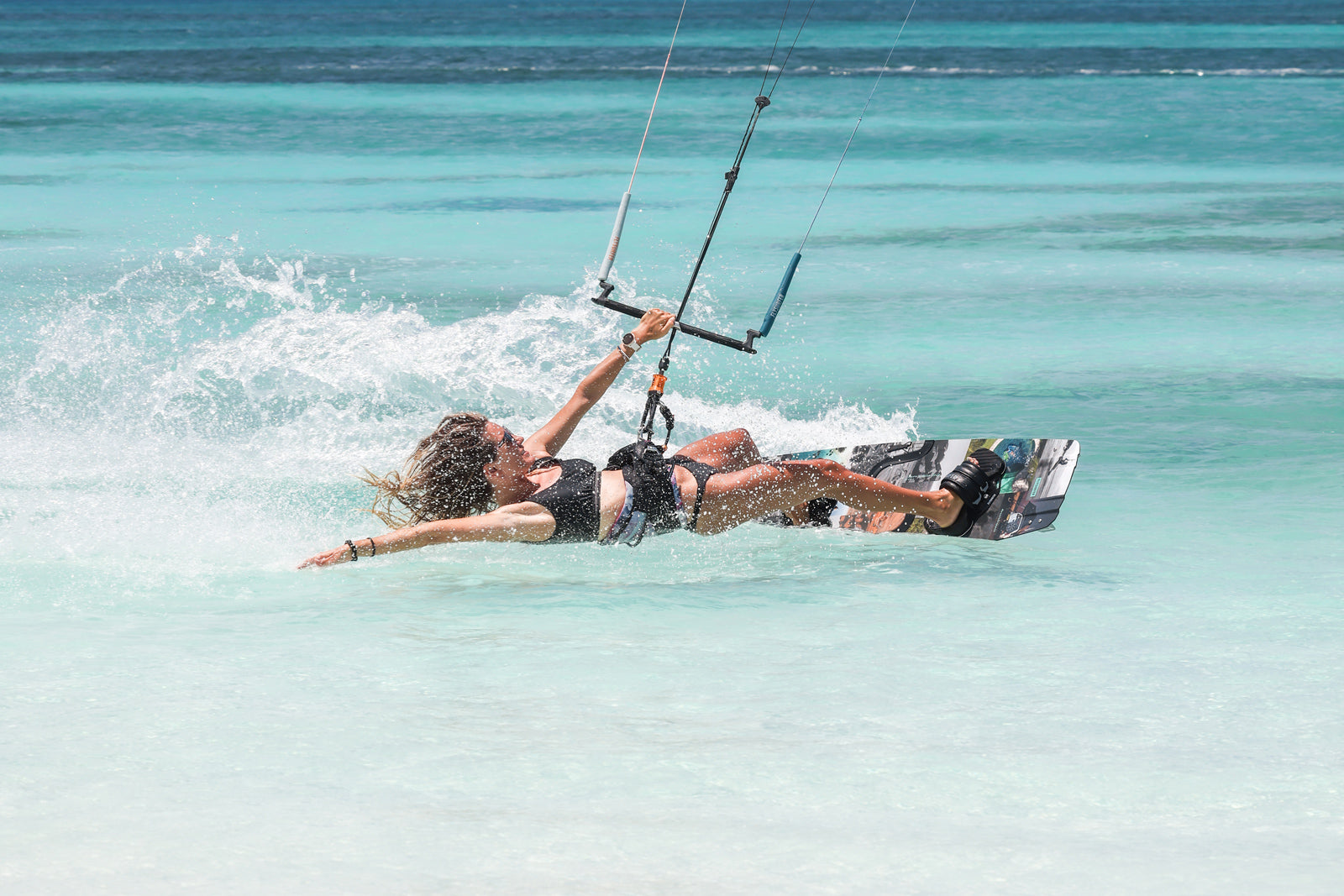 Kajtarka uživa na vodi z desko Flysurfer med sončnim dnevom na plaži.