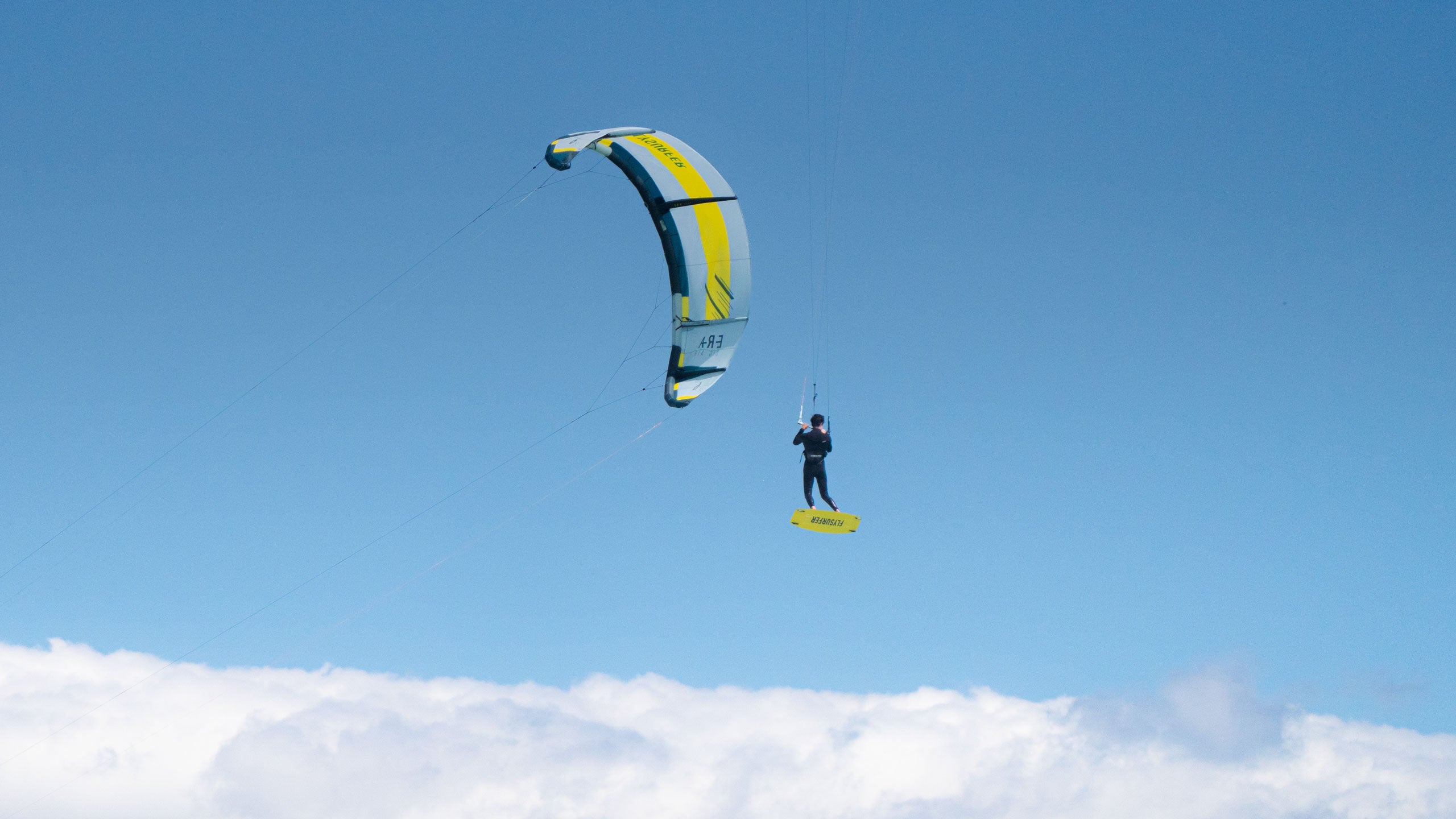 Kajtar med skokom z desko Flysurfer SHOT na modrem nebu – prikaz zmogljivosti deske v vetrovnih pogojih na odprtem morju.